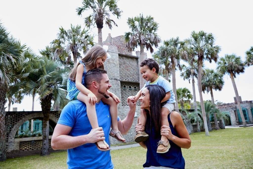 A mom and dad with their son and daughter sitting on their shoulders outside Atalaya Castle in the Hammock Coast