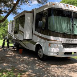 A large Georgetown motorhome with extended slide-outs parked at a shaded campsite