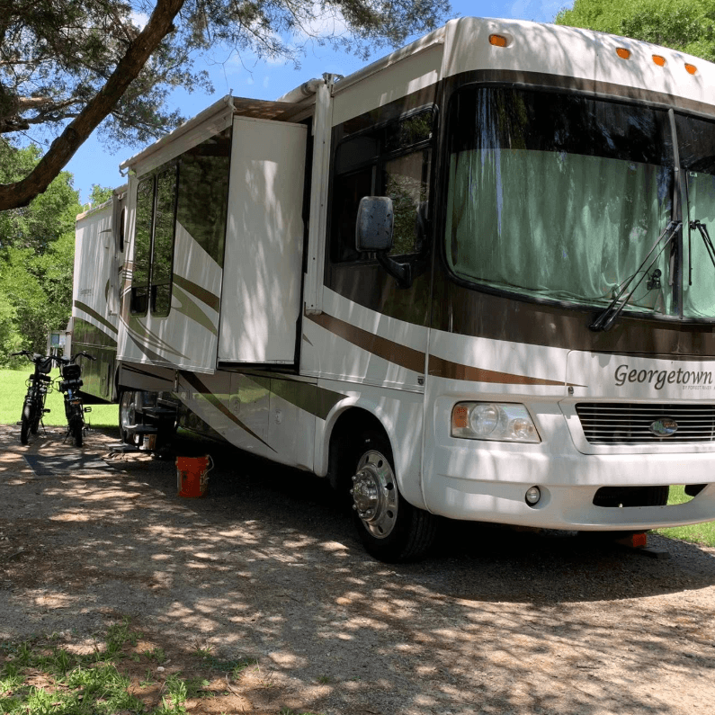 A large Georgetown motorhome with extended slide-outs parked at a shaded campsite